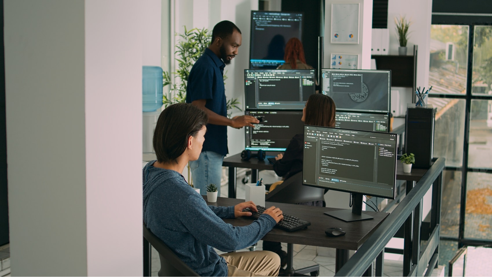Team of web developers collaborating in a modern office, focused on coding and software development, with multiple computer screens displaying programming interfaces.