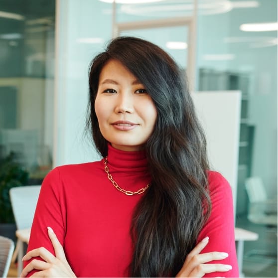 Confident woman in a red turtleneck sweater with long hair, standing in a modern office environment, representing Brandmode's innovative digital marketing solutions.